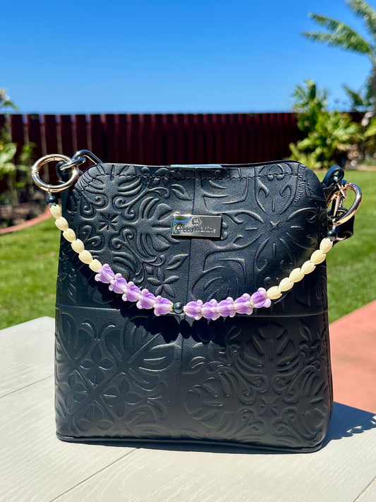 Black embossed handbag with a flower purse charm on a table outdoors